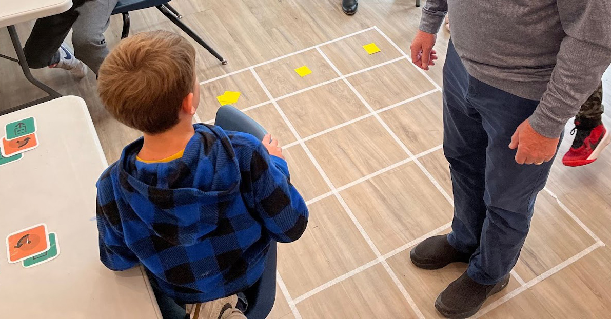 Modeling digital activities in the real world to help students understand the tasks Adult is moving on a grid based on a student instructions
